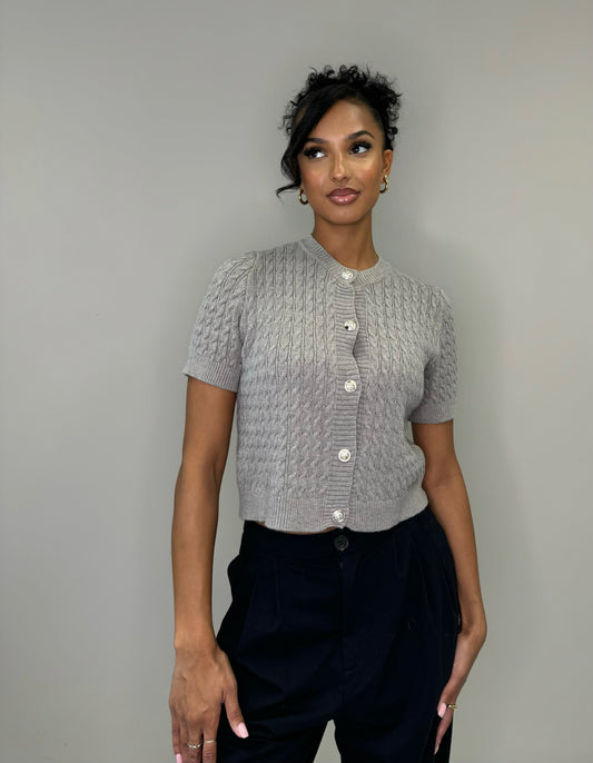 Model draagt een grijze cropped cardigan met korte mouwen en sierknopen.